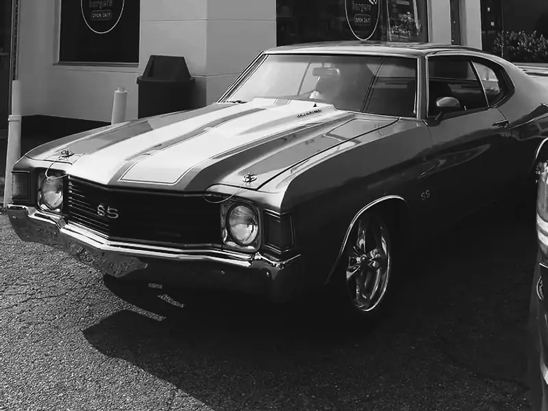 A classic Chevelle with racing stripes parked beside the white Better Burgers building on a sunny day (black-and-white print).