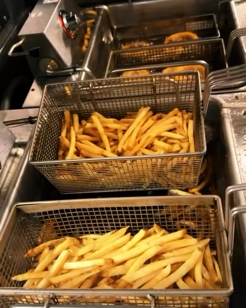 A steel fry basket full of golden french fries above the fryer.