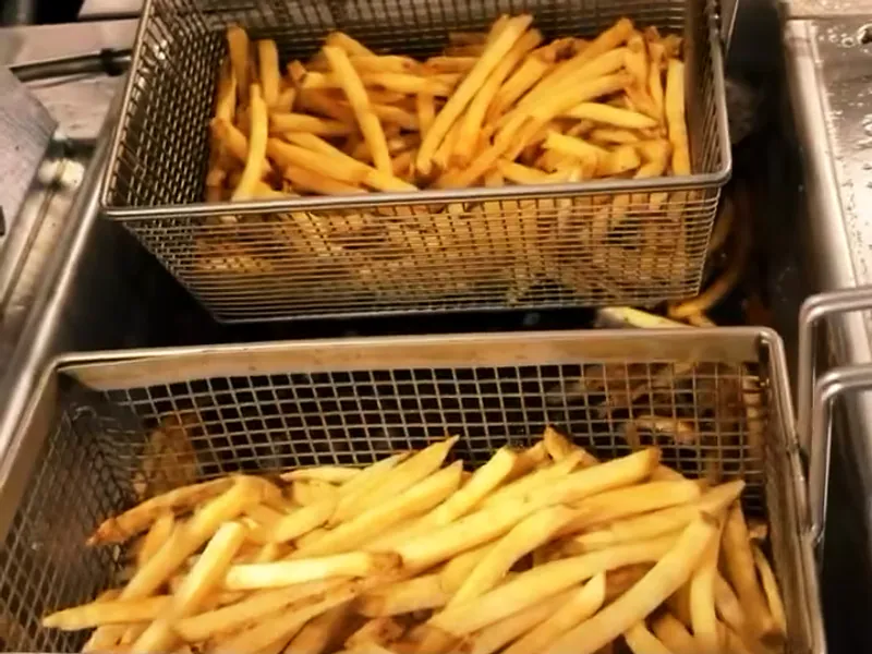 Two steel fry baskets full of golden french fries lifted above the fryer.