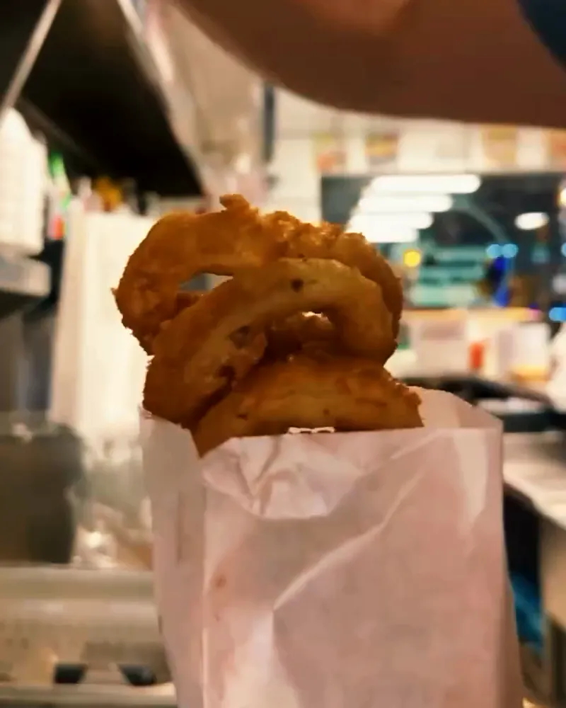 A stack of battered onion rings standing up out of a white paper bag, held up in the kitchen.