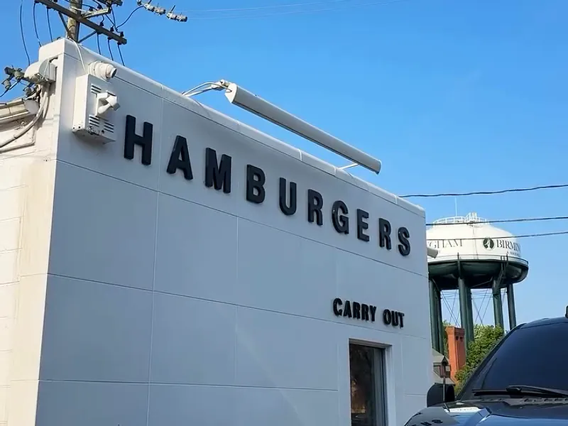 The white Better Burgers building in sunshine: black HAMBURGERS letters, a CARRY OUT sign and the Birmingham water tower behind.