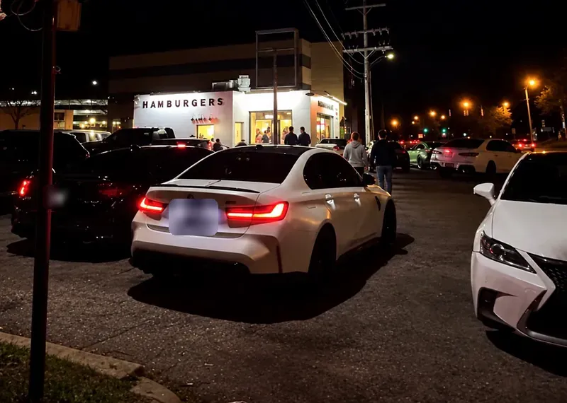 2:00 AM. The lit white HAMBURGERS building across a parking lot full of cars at night.