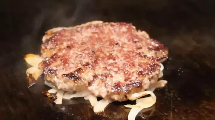 On the flat-top: a ball of beef under a pile of shredded onion, the press coming down, a thin lacy patty smashed onto its onions, then slices of American cheese laid on.